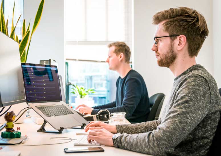 Dos personas trabajando en laptops en una oficina